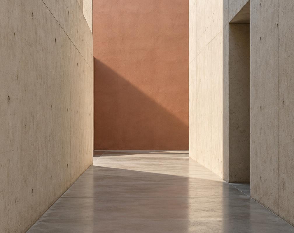 A concrete passage leading toward a sunlit terracotta wall